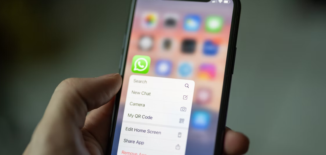 A hand holding a phone with WhatsApp on the screen.