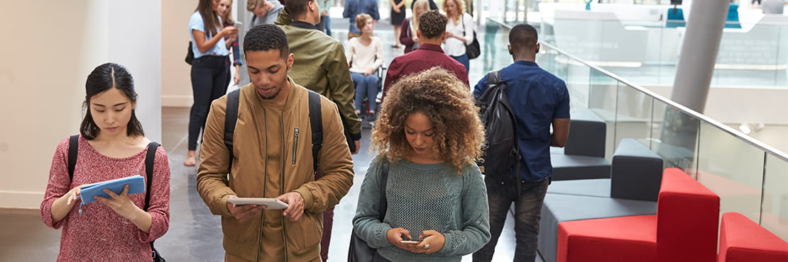 3 students walking side by side all looking down on their phones