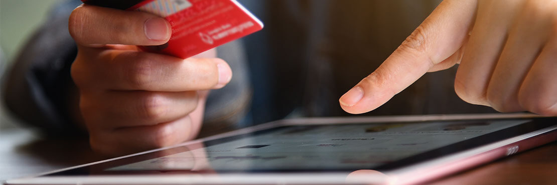A man holding a credit card on one hand and scrolling on an tablet